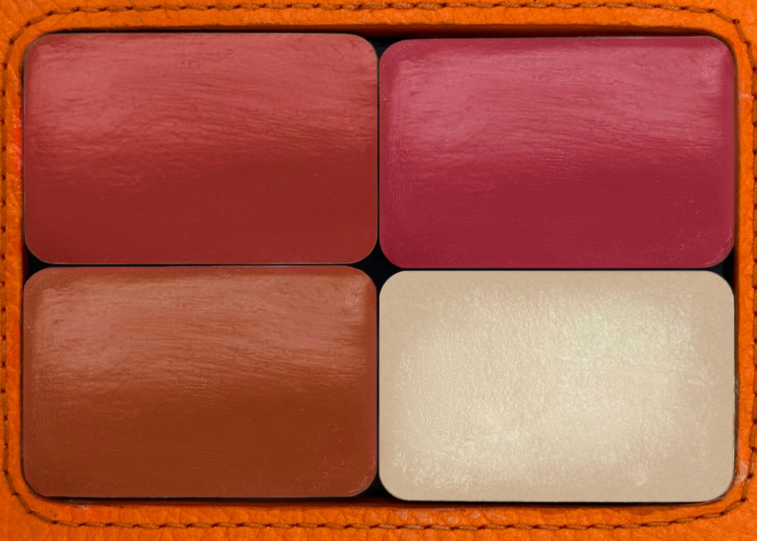 Four lipstick swatches in brown, red, and beige on a textured orange background