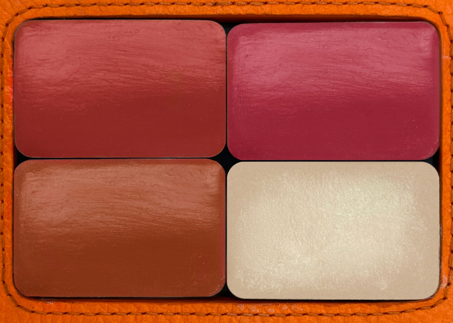 Four lipstick swatches in brown, red, and beige on a textured orange background